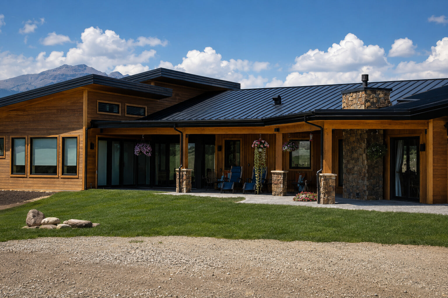 Completed courtyard side of the Arkansas Valley Residence with wood-toned siding, a dark standing-seam metal roof, stone columns, and deep covered outdoor spaces.