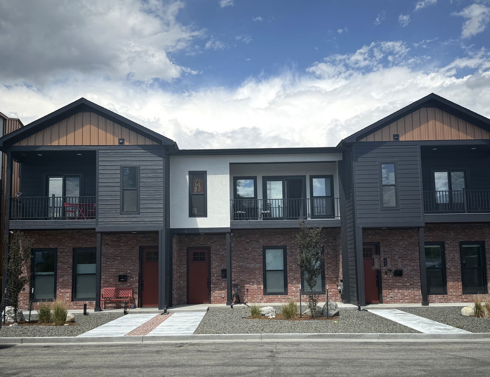 Completed photograph: Street view of Brickline Residences in downtown Salida with paired gables, recessed balconies, brick walls, dark siding, and warm wood-toned accents.