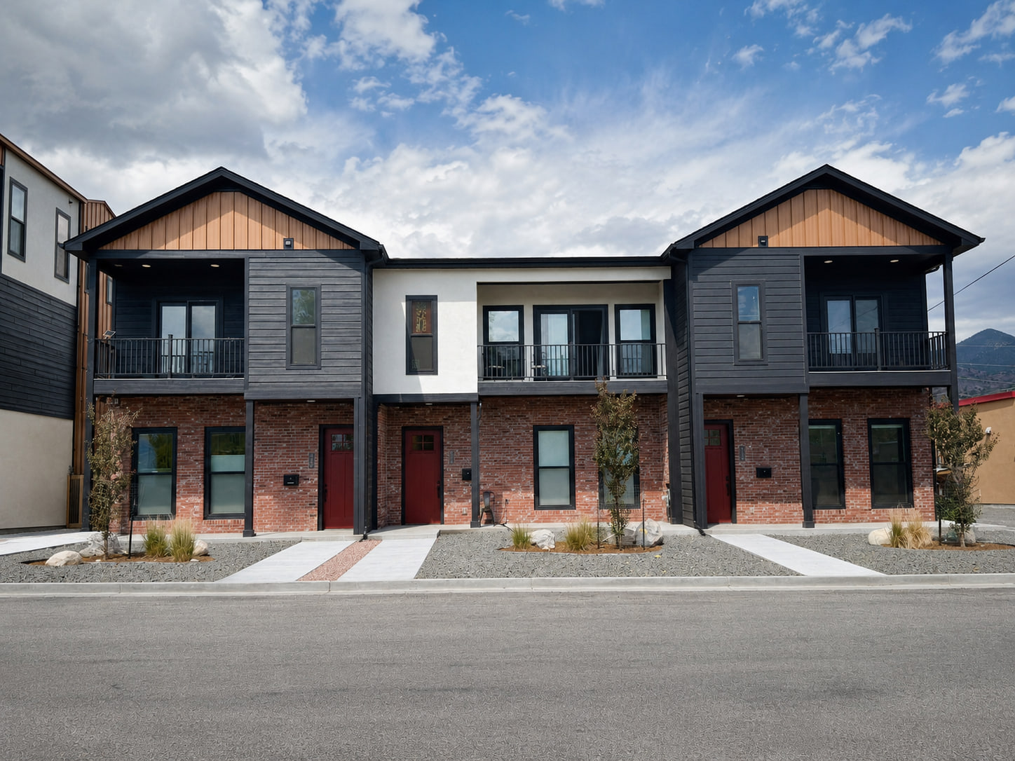 Centered front elevation of a contemporary Salida triplex with individual entries, upper balconies, brick lower walls, dark horizontal siding, and light stucco.