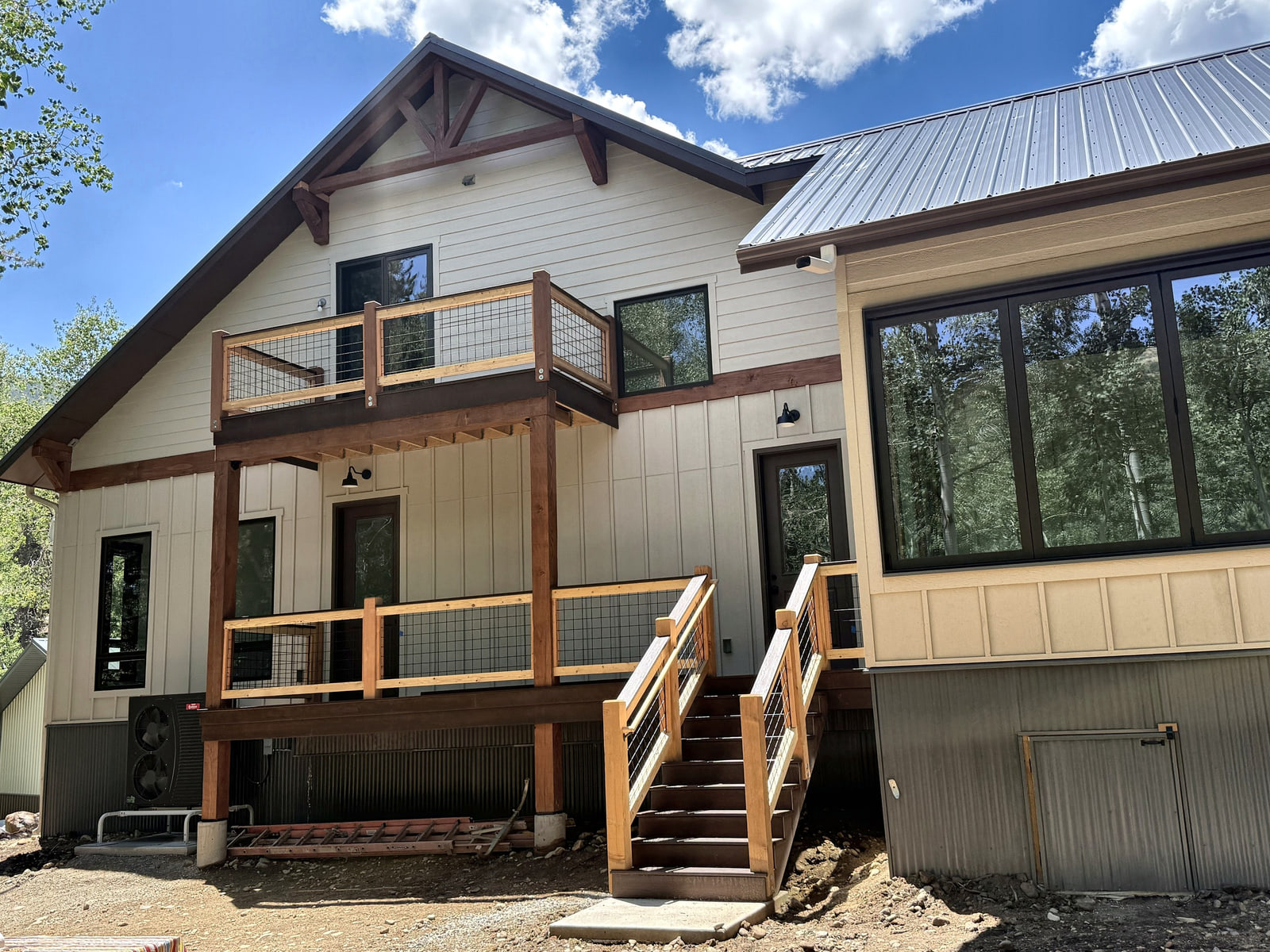 Rear elevation of the mountain home with an upper balcony, covered deck, exterior stairs, and large windows.