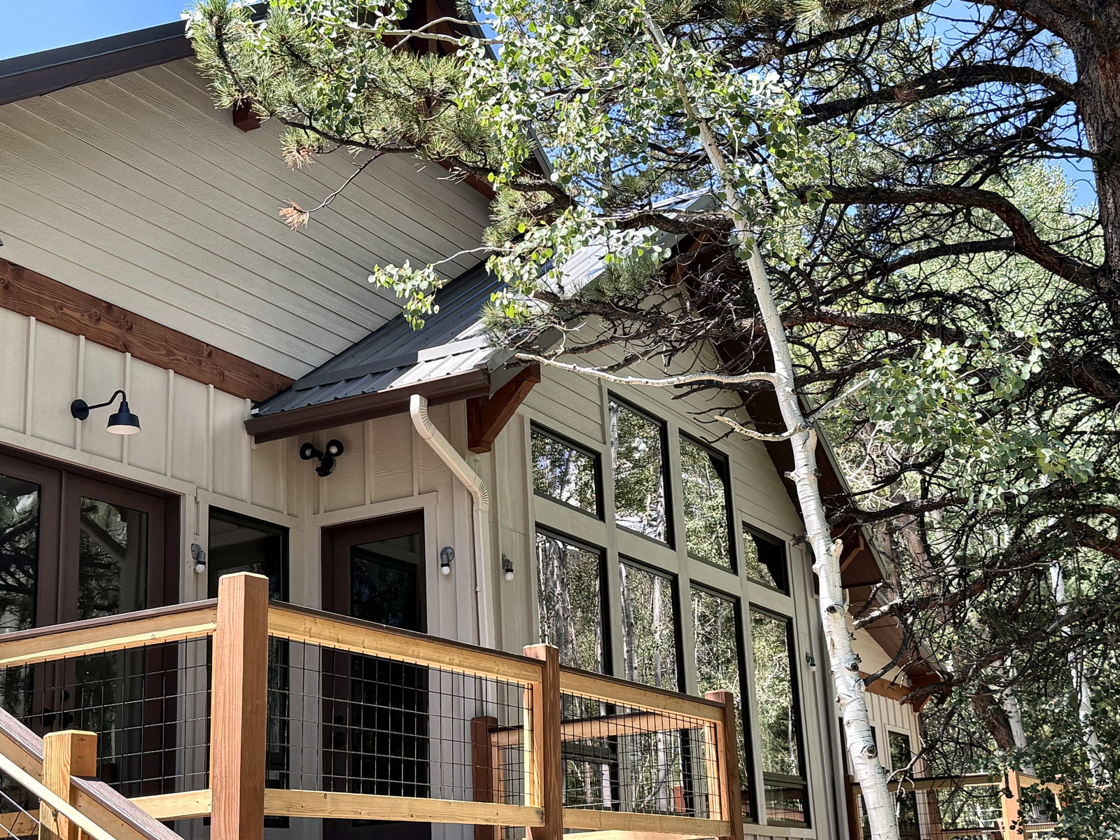 Exterior detail of a tall window wall and deck framed by mature mountain trees.