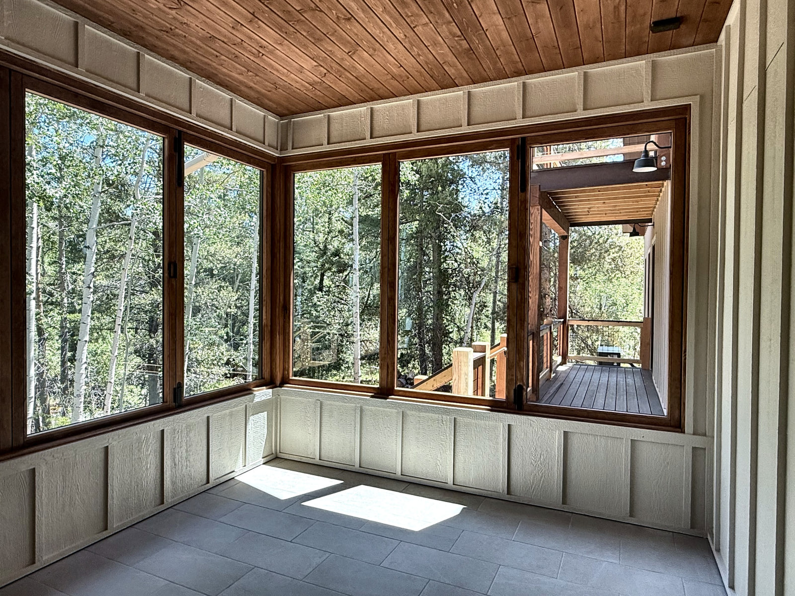 Screened porch with wood ceiling, corner glazing, light wall paneling, and views into the trees.