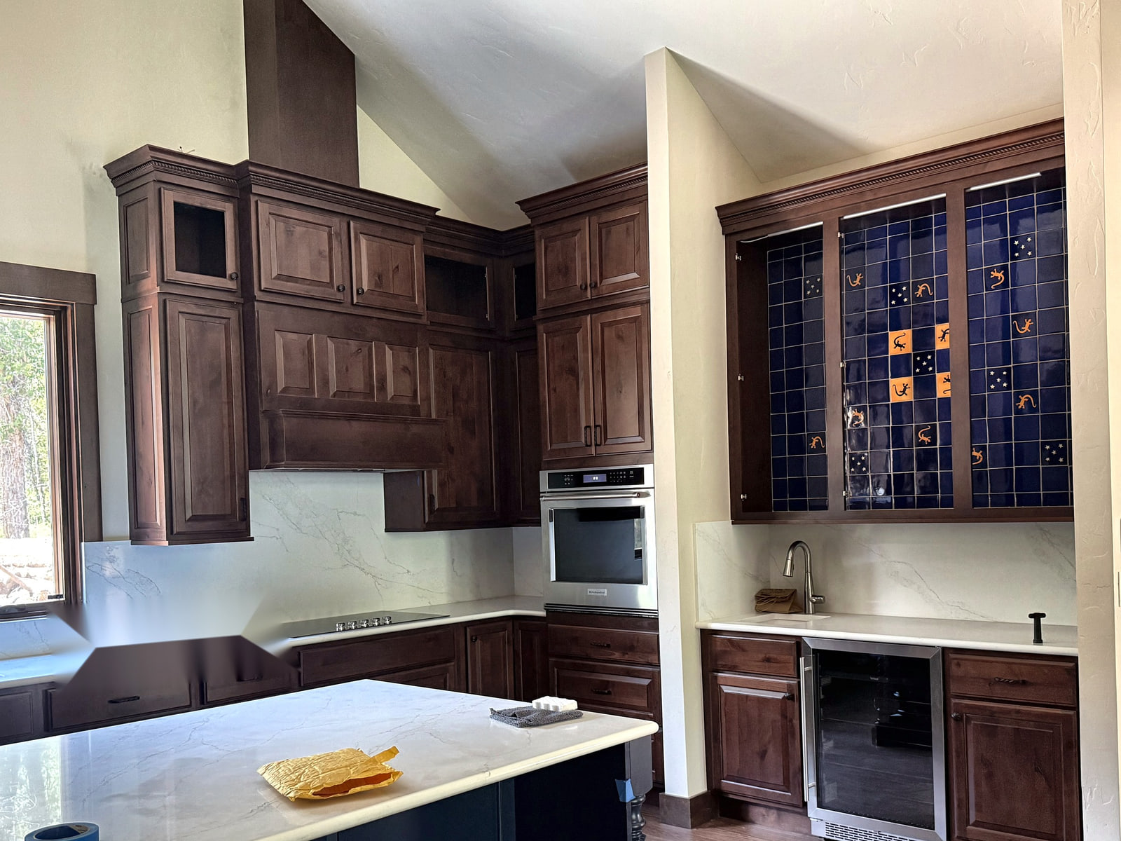 Custom kitchen with dark wood cabinetry, white counters, contrasting island, and blue accent tile.