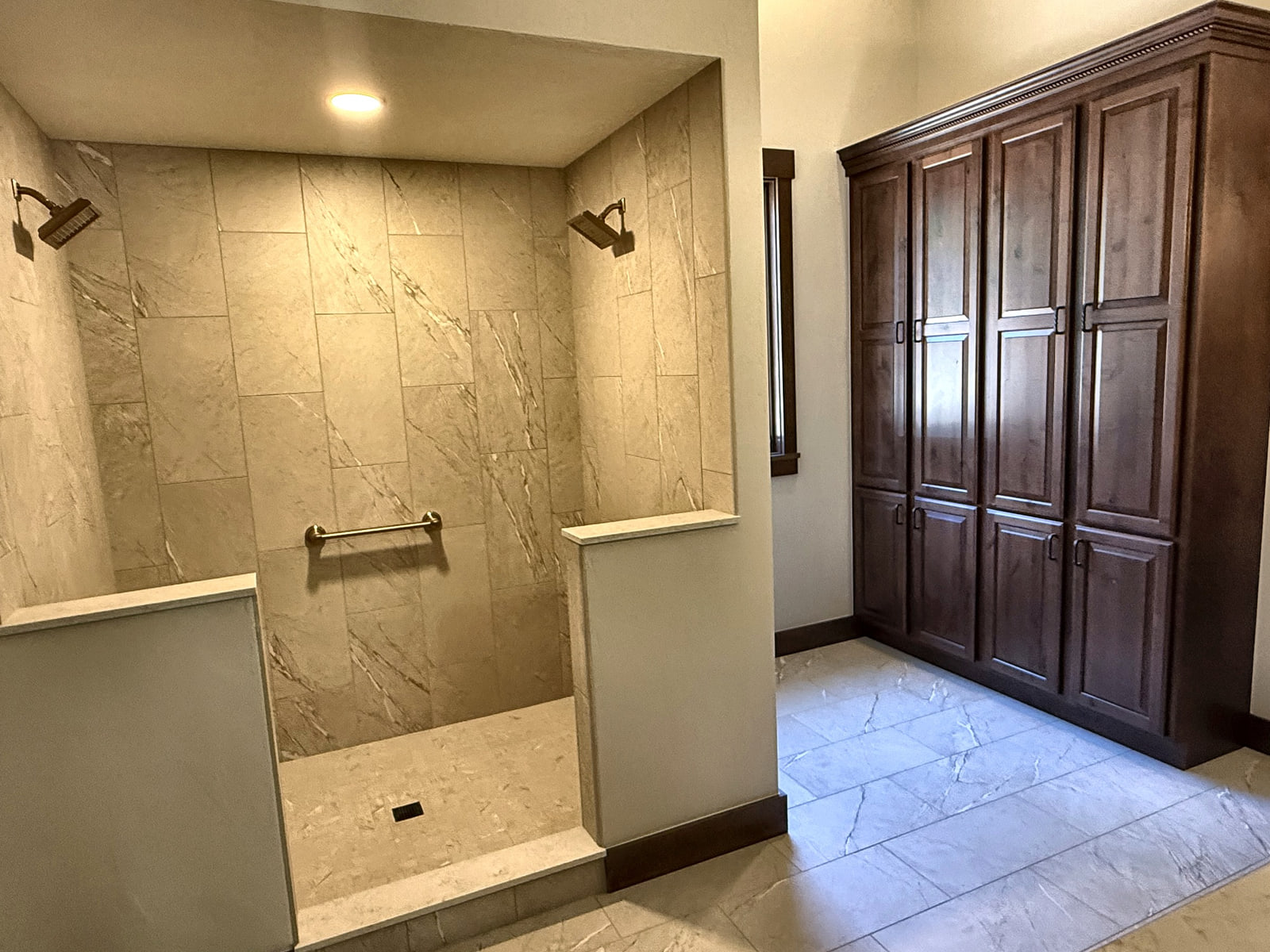 Primary bathroom with a large tiled walk-in shower, light stone floor, and tall dark wood cabinetry.