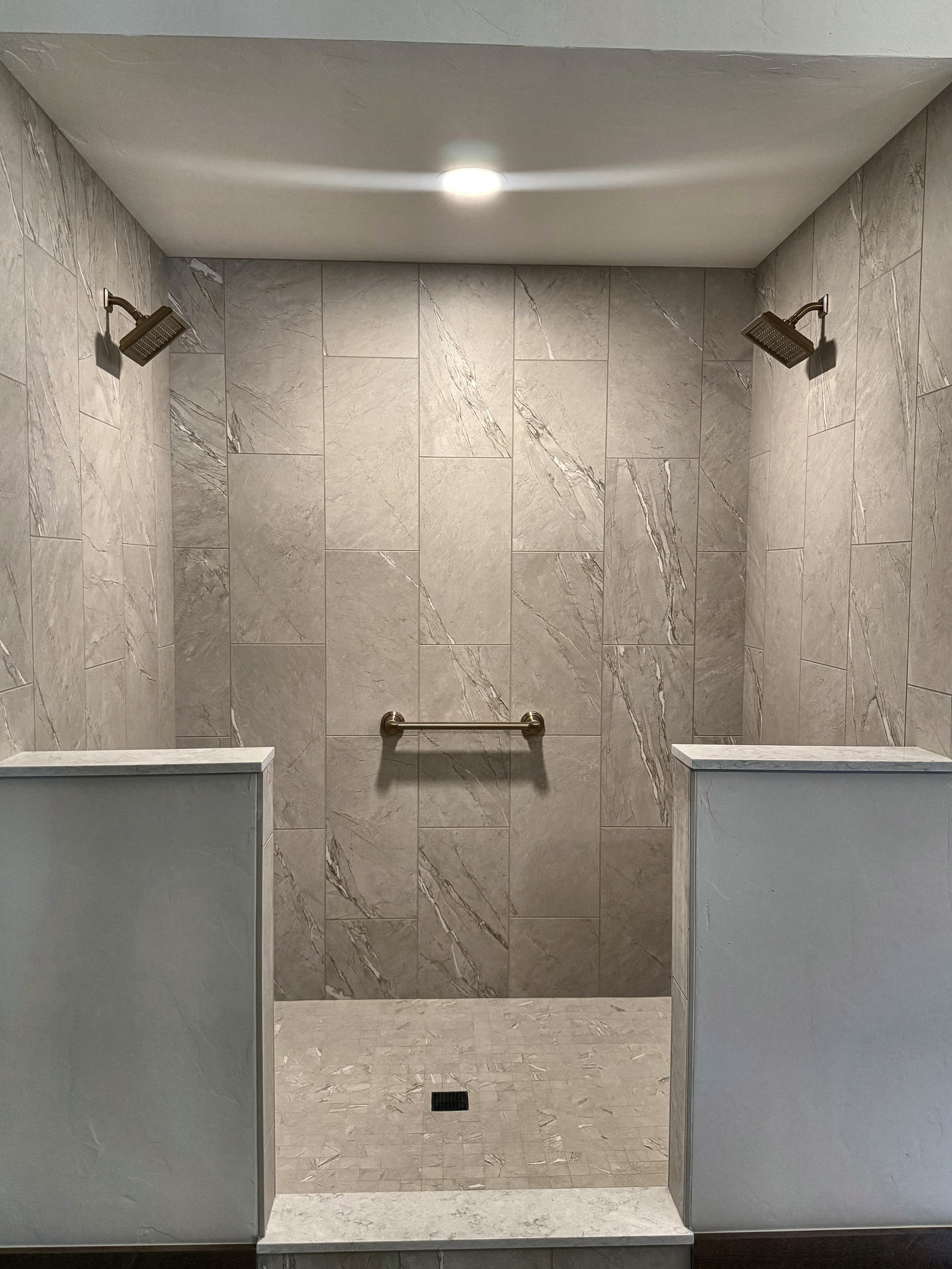 Detailed front view of a tiled walk-in shower with dual shower heads and grab bar.