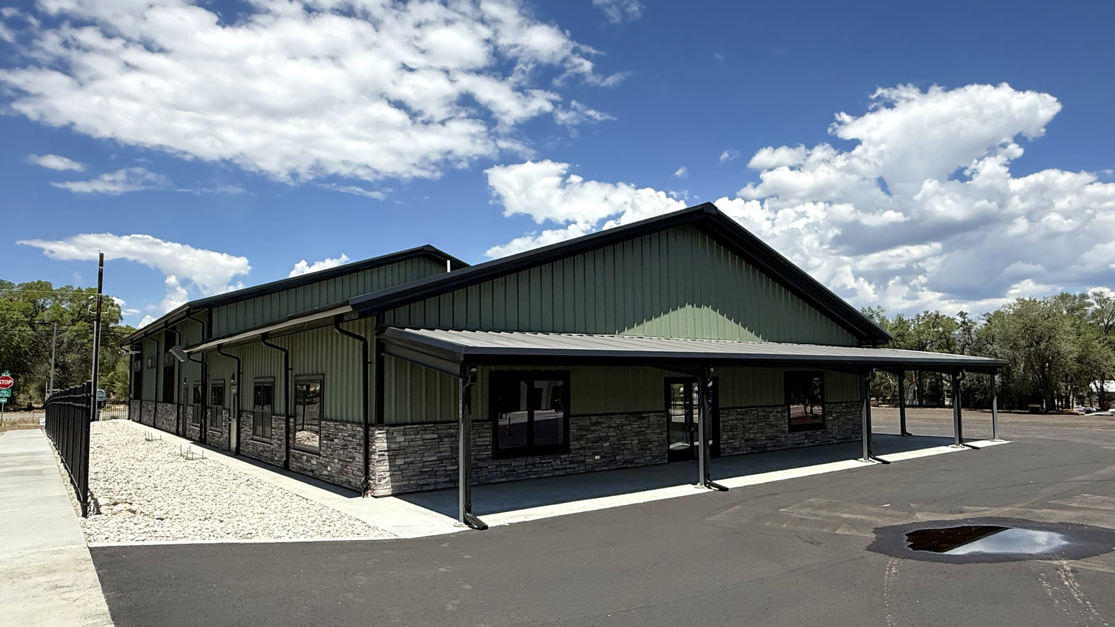 Completed photograph: Front and side view of Iron Mountain Tool & Equipment Rental from the parking-lot approach, showing green metal siding, stone accents, layered roof forms, and covered walkways.