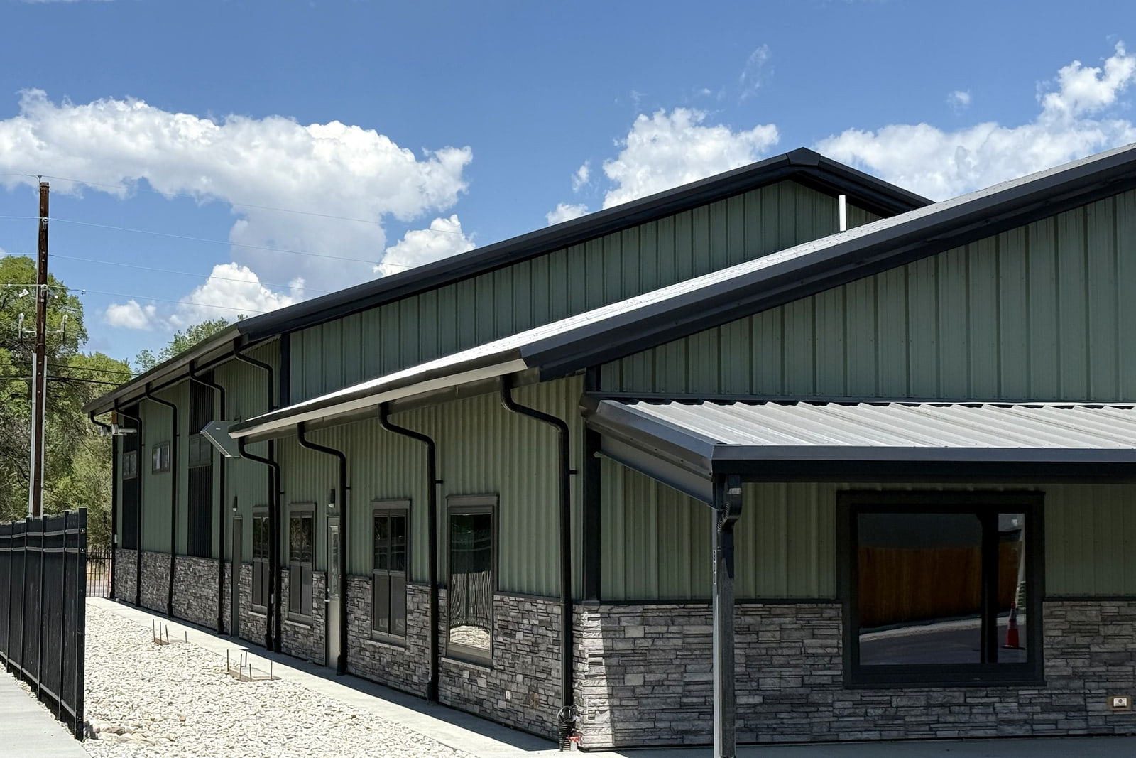 Architectural detail showing green metal siding, stone veneer, dark trim, windows, and the covered pedestrian walkway.
