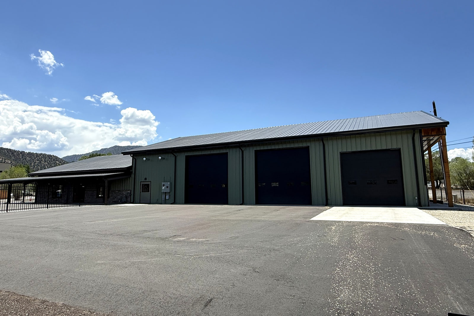 Equipment-maintenance building with three large overhead service-bay doors and an attached covered area.