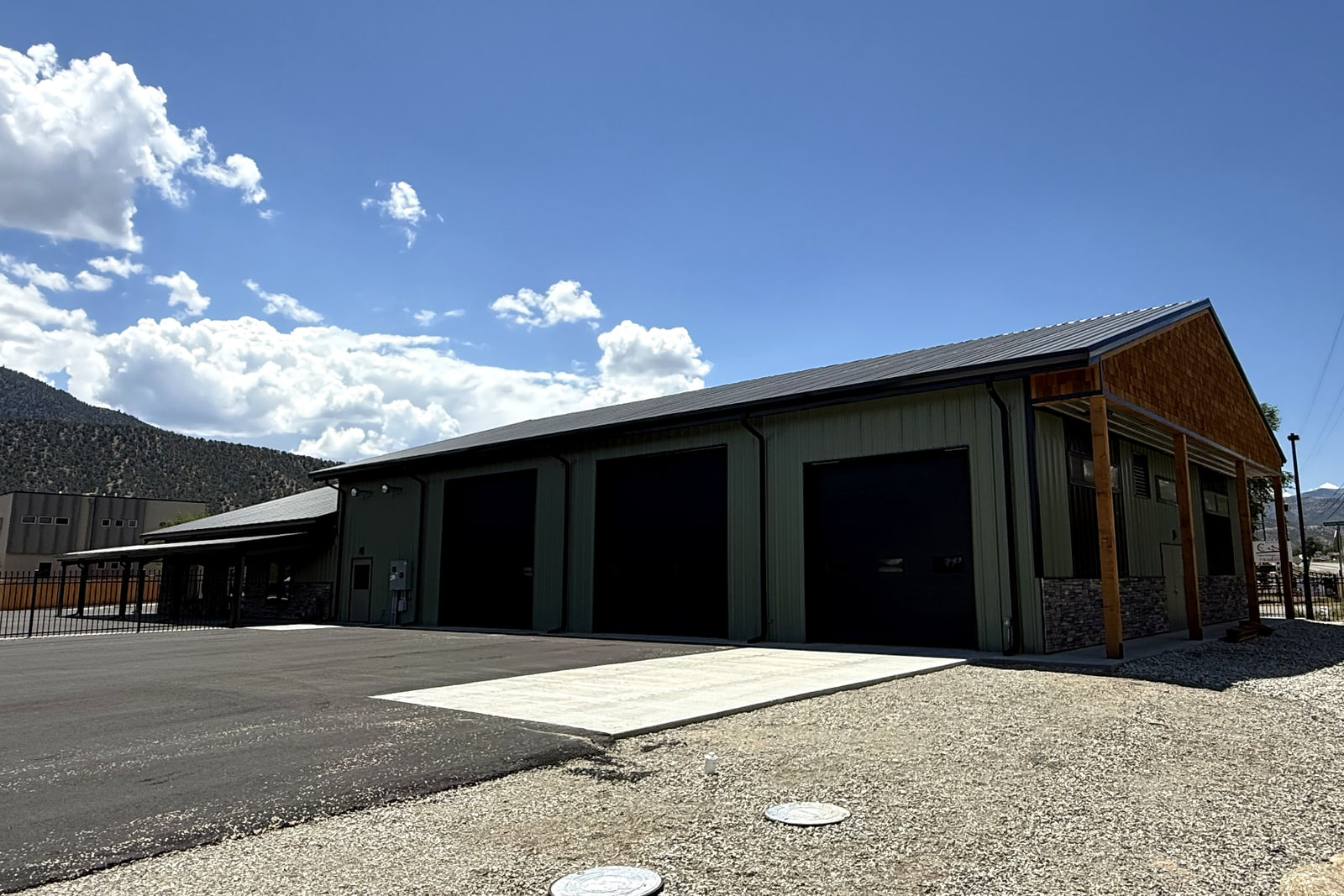 Service end of the equipment-rental building with large overhead doors, timber framing, and surrounding mountain views.