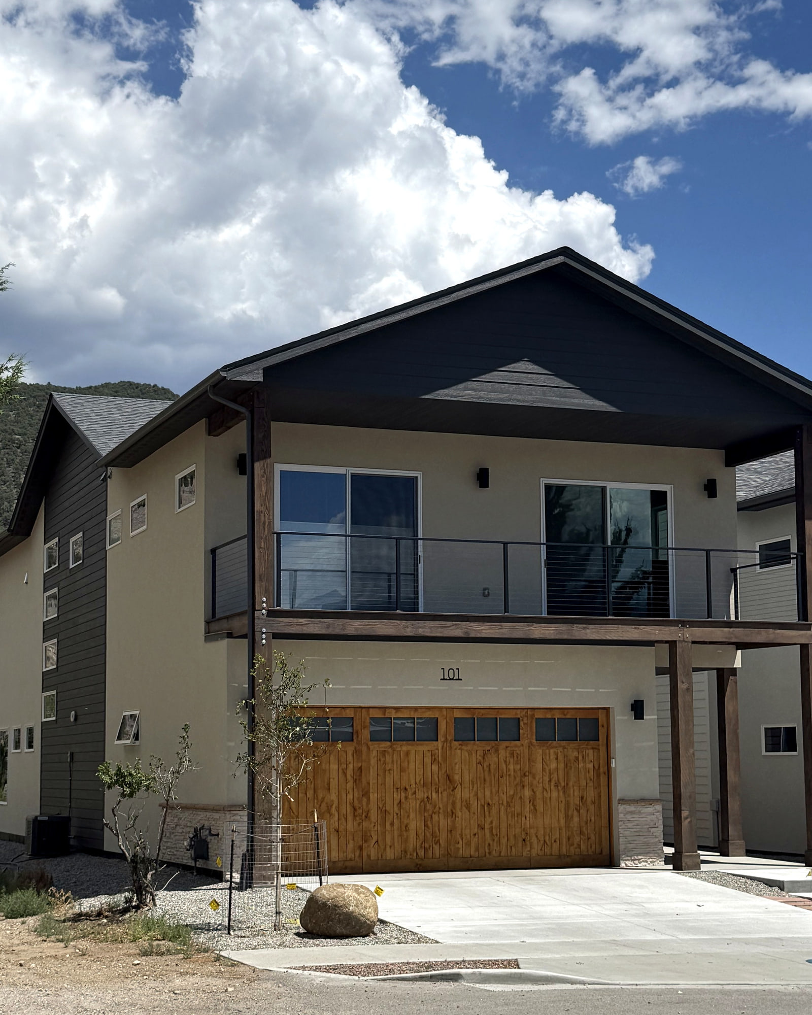 Angled street view of a contemporary Salida home with a deep gabled roof, wood garage door, and second-floor deck.