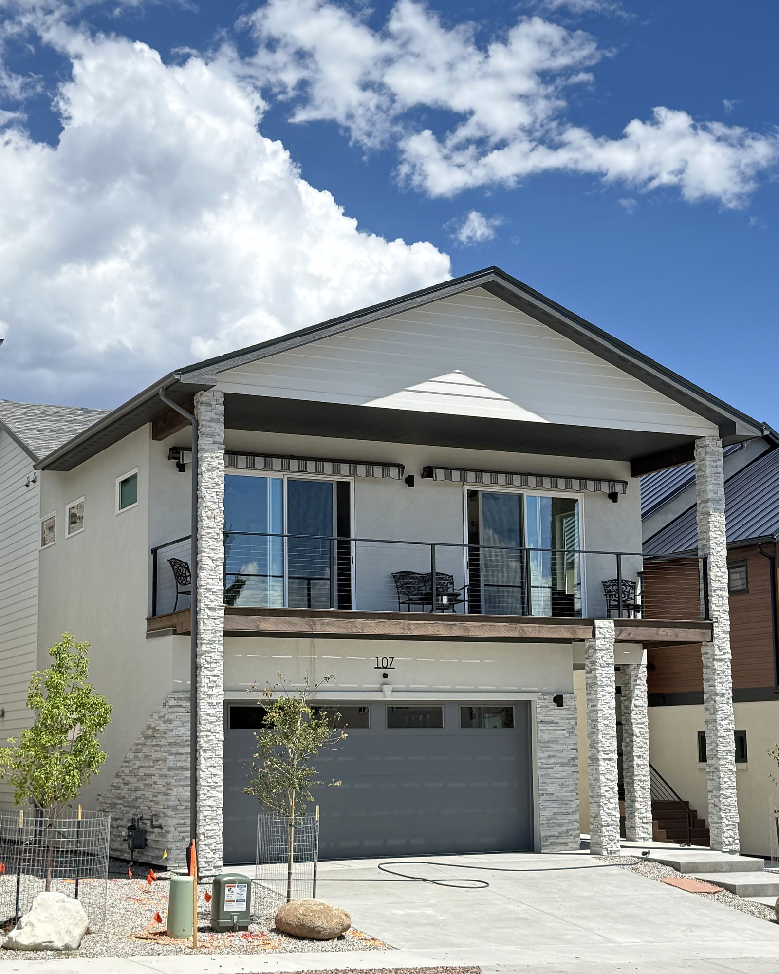 Street-facing view of a light-colored contemporary home with stone-clad columns and an elevated outdoor deck.