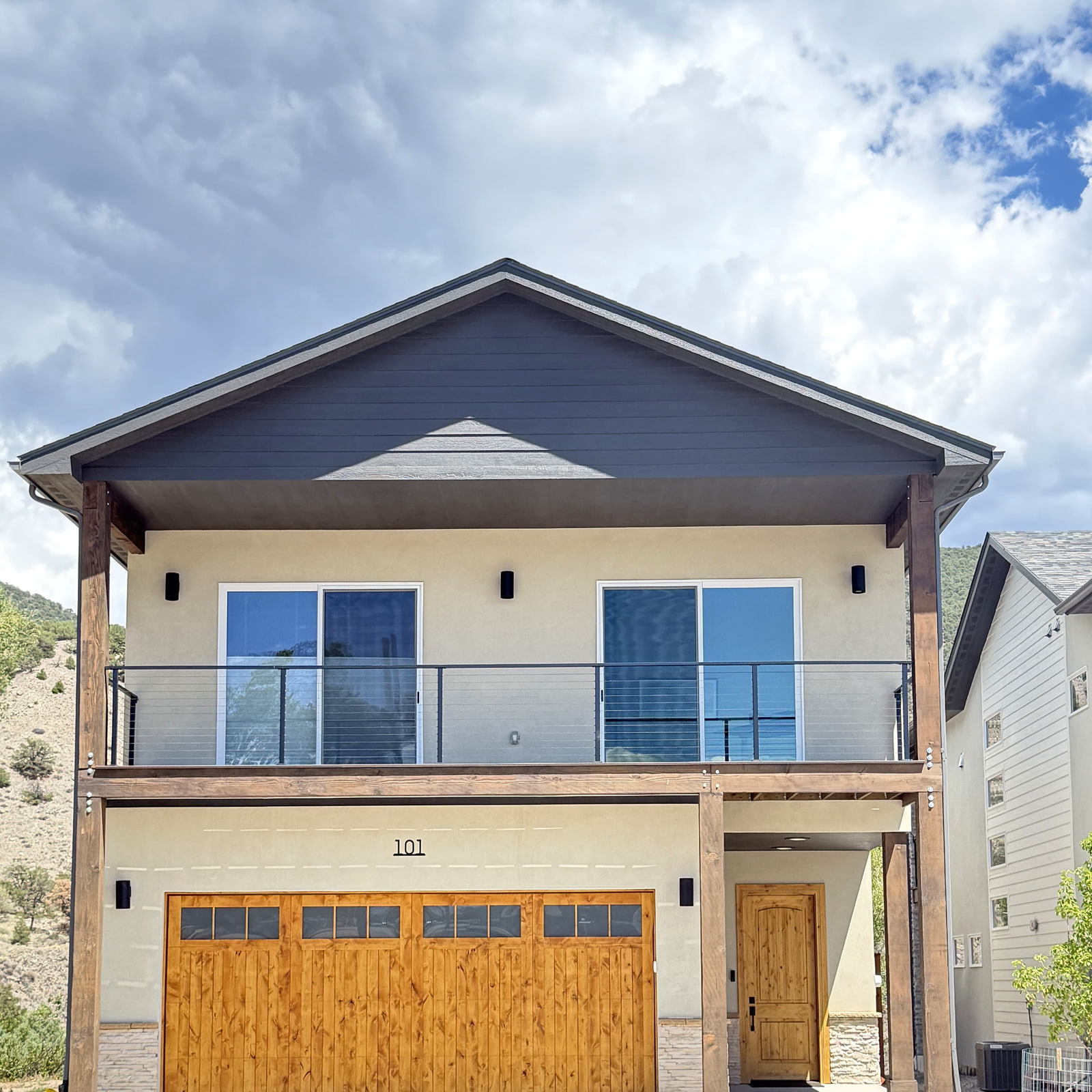 Front architectural view of a contemporary mountain home with timber accents and a broad upper-level deck.