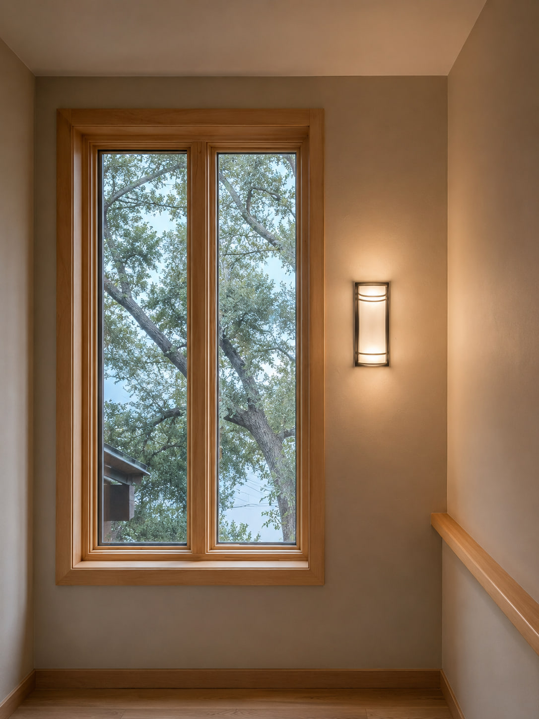 Wood-trimmed stairwell window with tree views and a wall sconce.