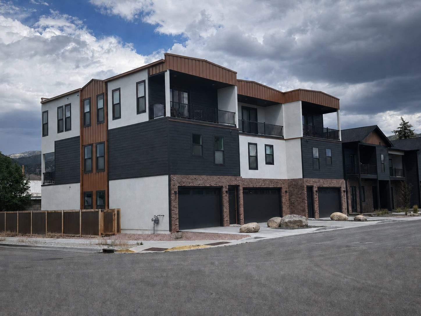 Completed photograph: Corner perspective of a modern downtown Salida triplex with brick at the base, dark siding, light exterior walls, and covered upper terraces.