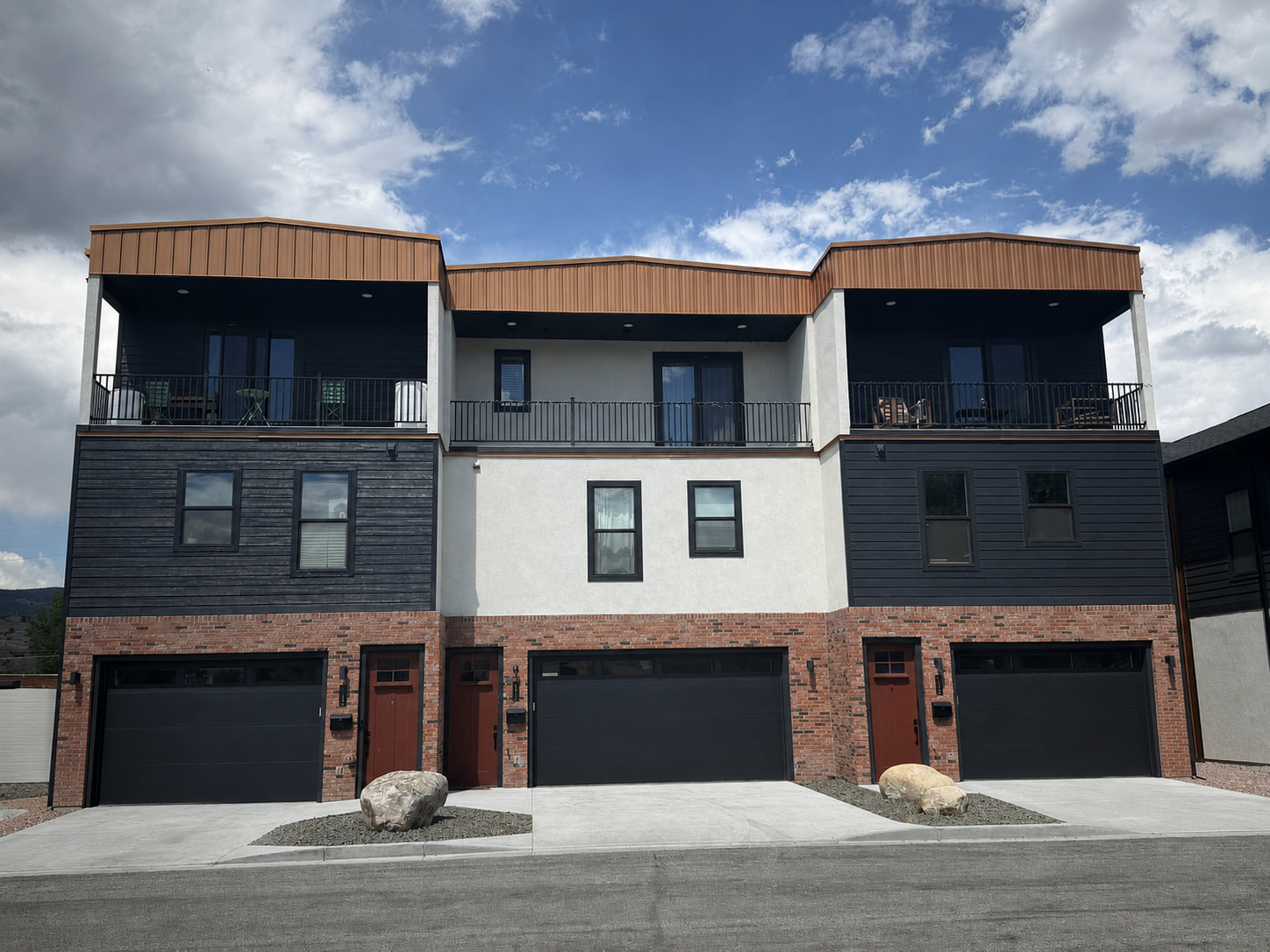 Straight-on rear elevation of the triplex with three garage bays, upper balconies, and a contemporary material palette.