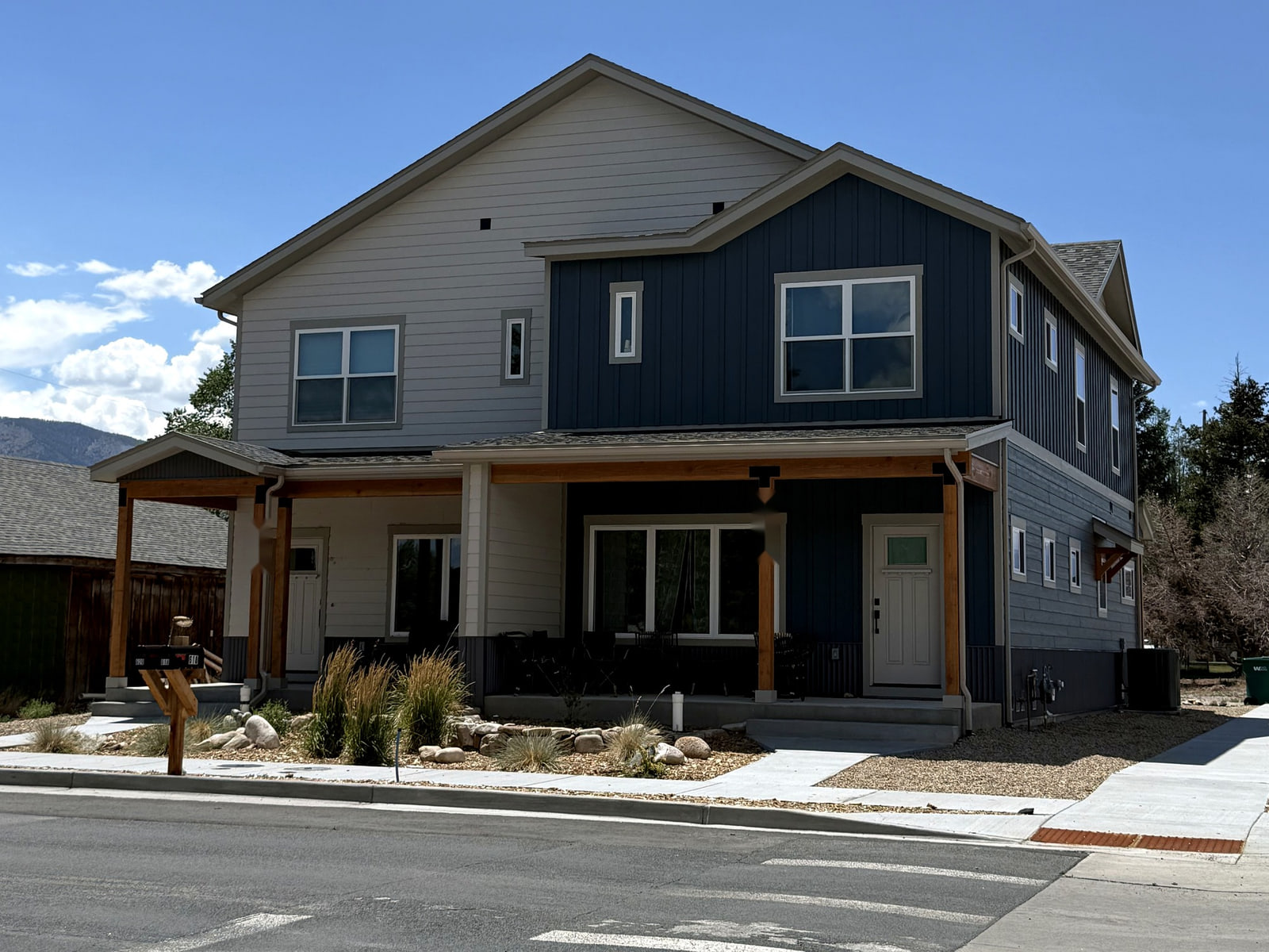 Completed photograph of the Shaken Roost Duplexes showing a two-story Salida duplex with gray and blue siding, exposed wood porch posts, and paired entrances.