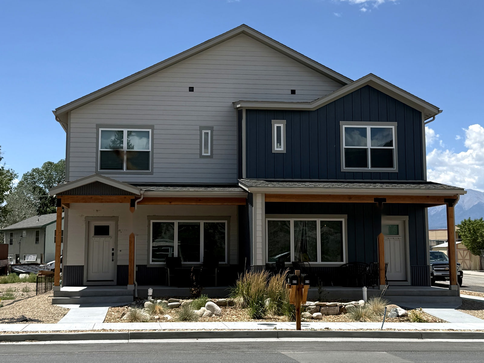 Front elevation of a duplex with two individual entrances, contrasting siding, gable roofs, covered porches, and low-water landscaping.
