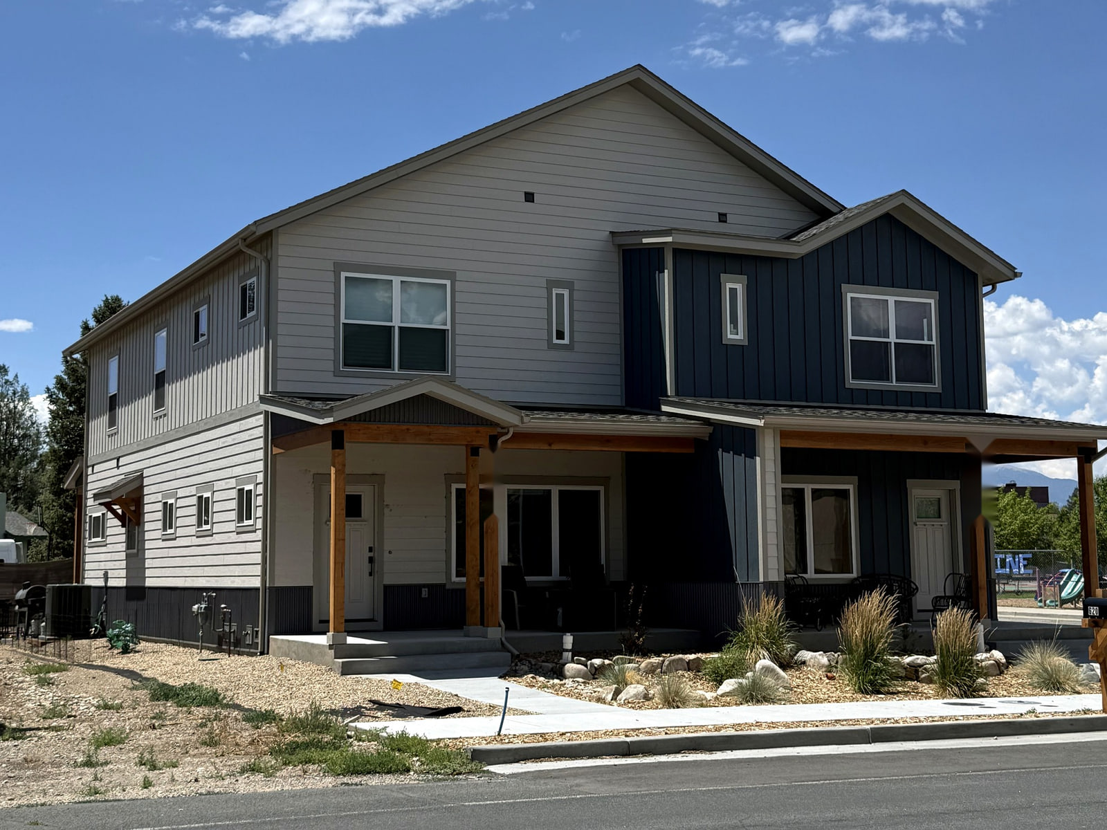 Opposite corner view of a two-story duplex showing varied siding, porch elements, and the articulated side elevation.