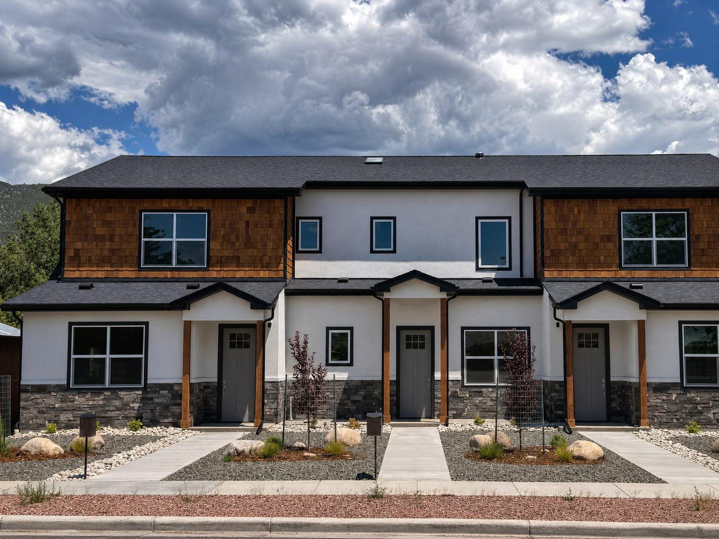 Completed photograph: Front elevation of Three Gables Residences in Salida, featuring three individual entries, wood accents, stone bases, and mountain landscaping.