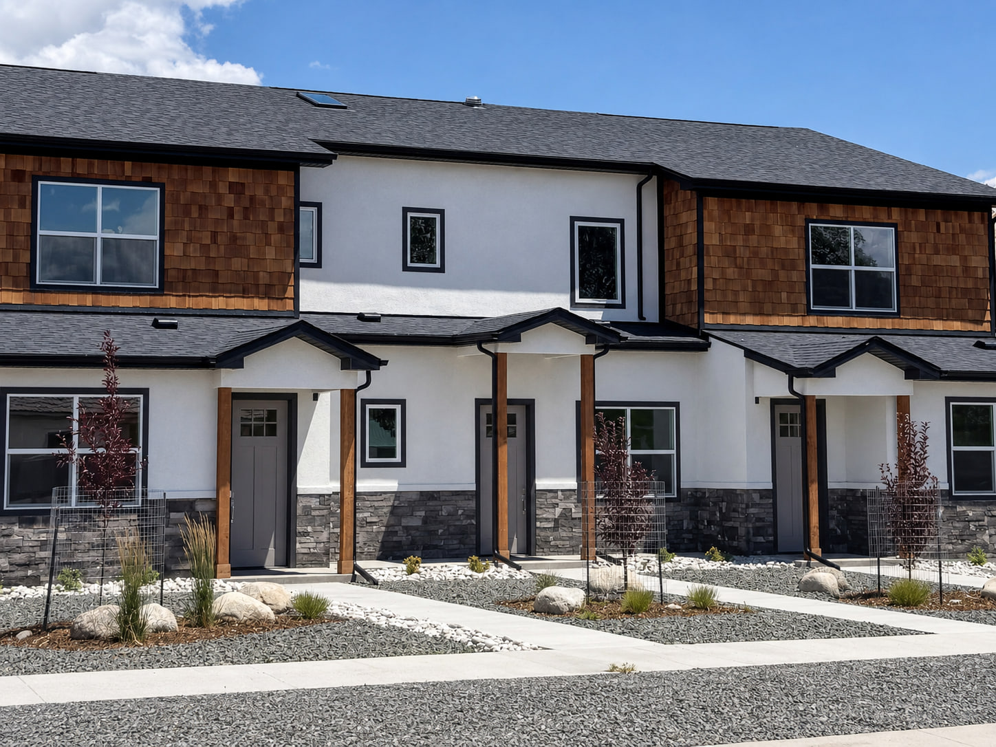 Full street-facing facade of a three-residence infill project with repeating porches and contemporary mountain materials.