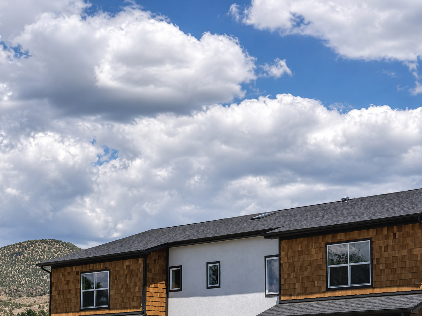 Upper facade and roofline of Three Gables Residences beneath dramatic clouds with a mountain visible beyond.