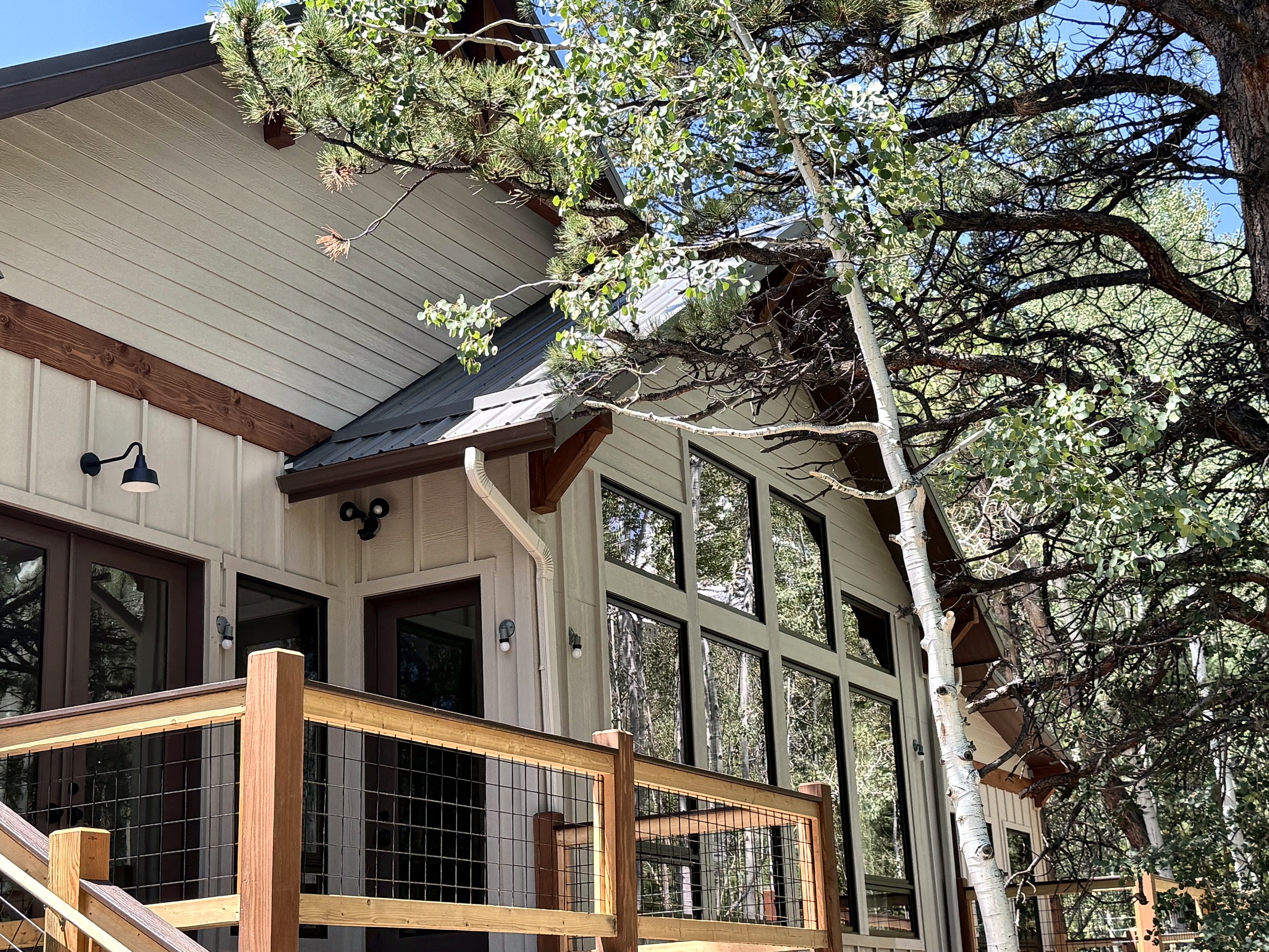 Exterior detail of a tall window wall and deck framed by mature mountain trees.