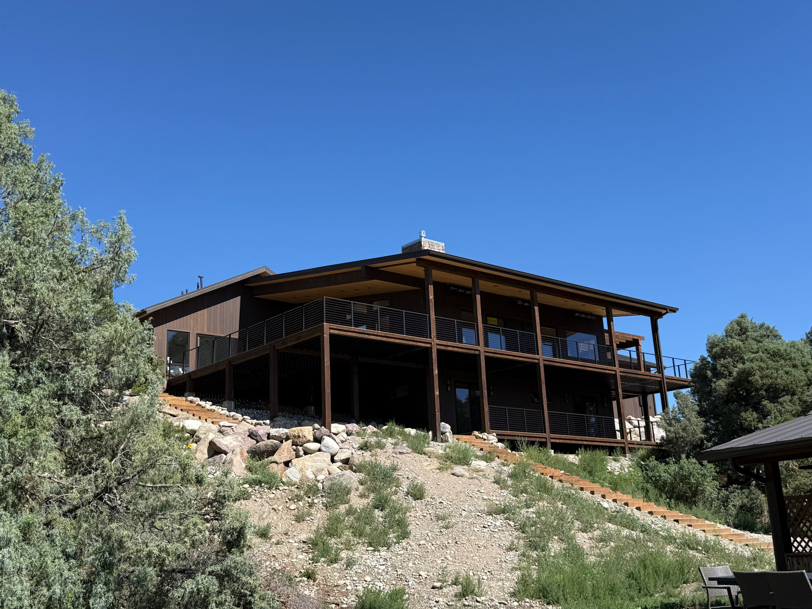 Low-profile riverside residence with deep covered decks and a dark wood-and-metal exterior palette.