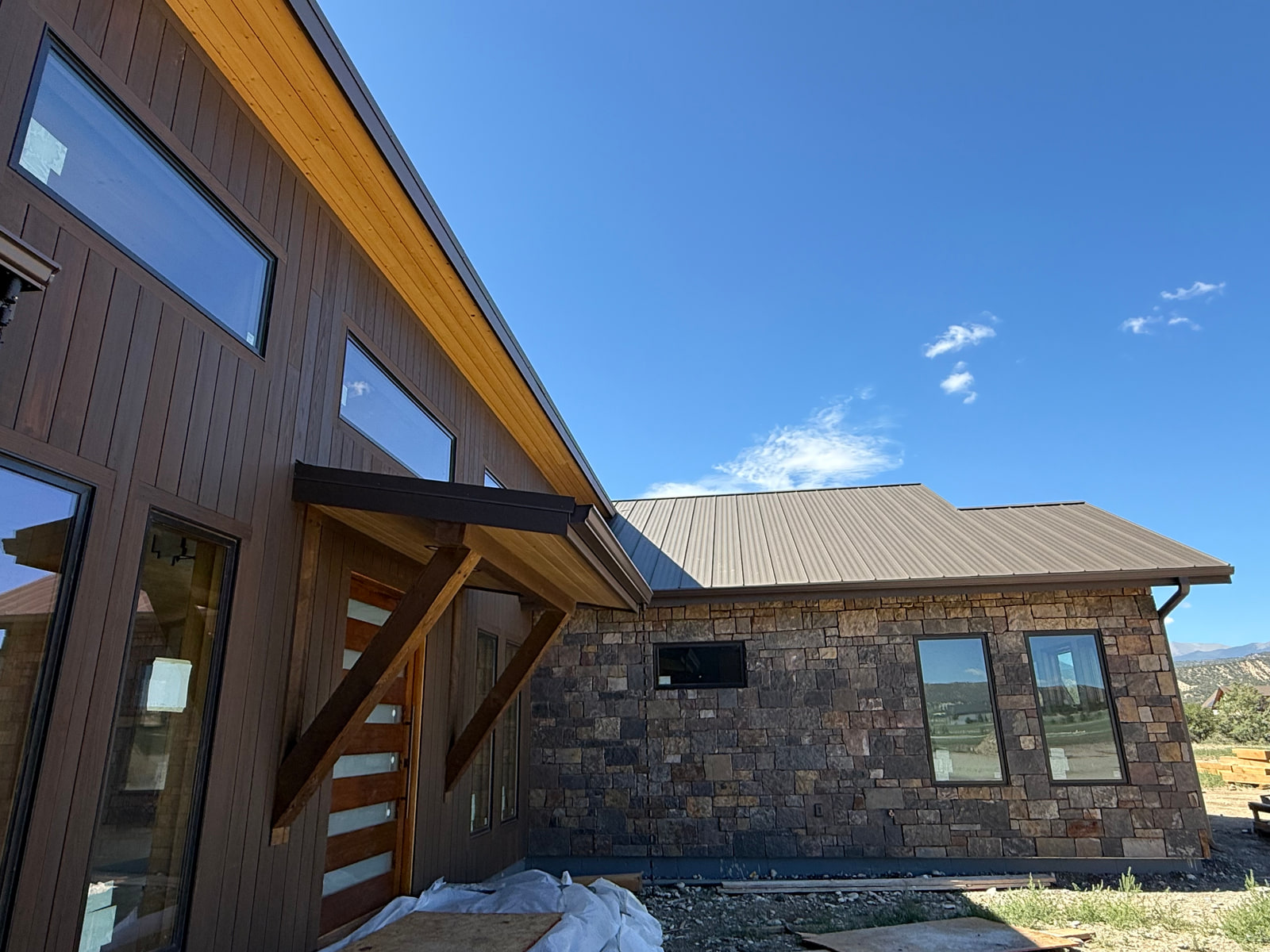 Timber-braced front entry between dark wood siding and stone cladding at Riverside Boathouse Overlook.